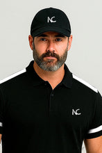 A man wearing a black baseball cap and matching black polo shirt with white stripe details and a white 'NC' logo, photographed against a light gray studio background.