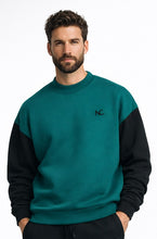 Man wearing a teal and black sweater with a logo on a white background