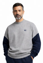 Man wearing a gray and navy sweater with a logo on a white background