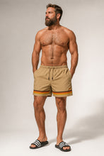 Man wearing csmel shorts with a striped drawstring on a plain background