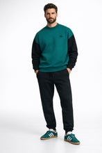 Man wearing a green and black sweater with black pants on a white background