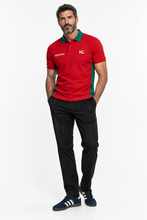 A man modeling a red short-sleeve polo shirt with green collar and side panels, featuring white 'PORTUGAL' and 'NC' logos on the chest, paired with black trousers and navy blue sneakers, against a plain white studio background.