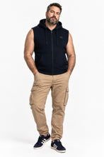 A man modeling a sleeveless black zip-up hoodie vest, paired with tan cargo pants and navy sneakers, against a plain white studio background.